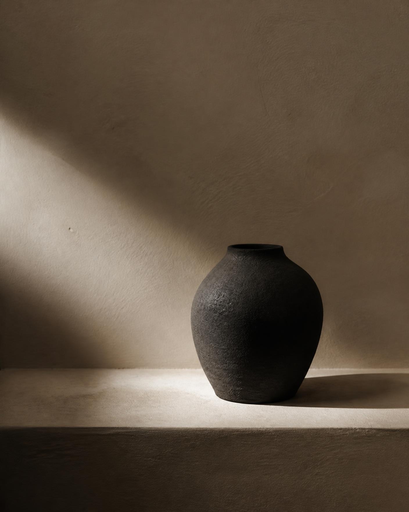 A single dark vessel on a warm ivory plaster ledge